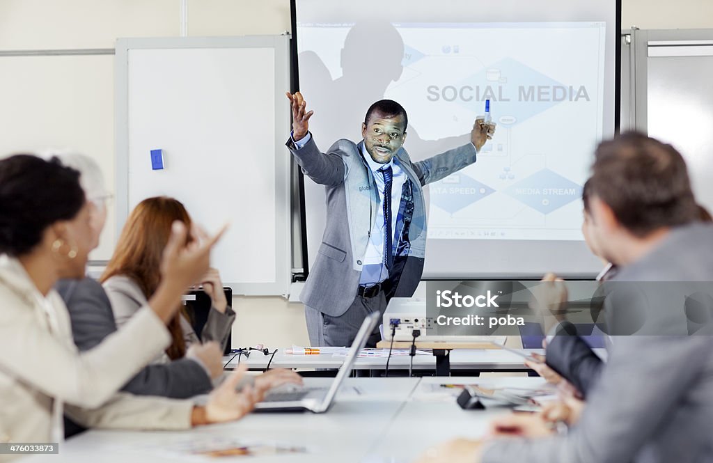 businessmen talking  in front of the business executives Business executives in a training class. Laptop and projector on the table.  people in the foreground. Shallow DOF. Lecturer using digital projector. Businessman explaining in front of projection screen Adult Stock Photo