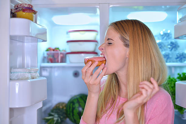 istock Woman eating a donut at night 476034150