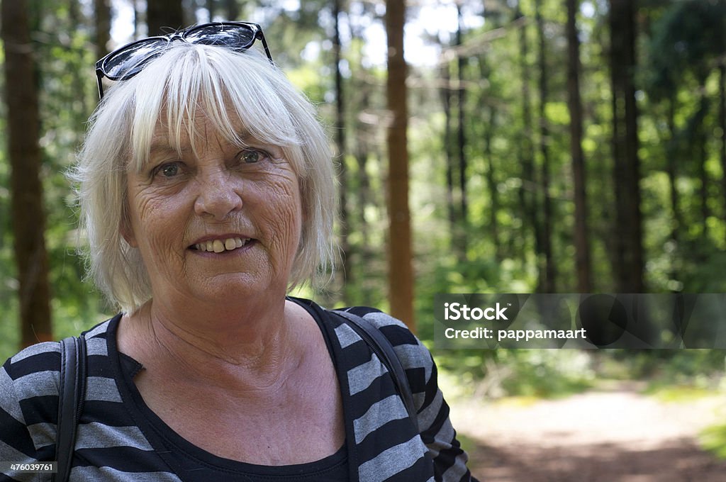 Happy senior woman posing in forest woman,female,senior,adult,happy,smiling,laughing,friendly,horizontal,color,one,striped,cardigan,trees,sunspots,white,gray,nature,forest,wood,posing,looking at camera,head and shoulders,sunglasses,stems,leaves,selective focus,focus on foreground Active Seniors Stock Photo
