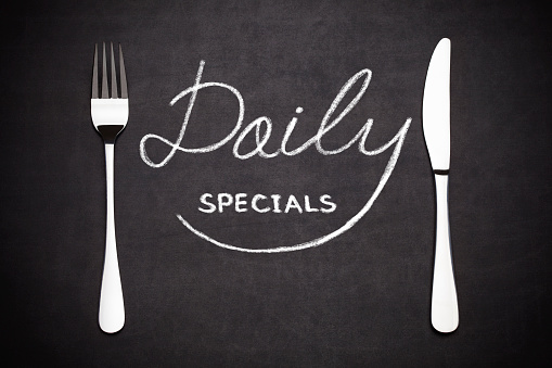 Daily specials lettering , with a fork and a knife on the side  drawing with chalk on blackboard.