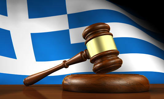 Law and justice of Greece concept with a 3d rendering of a gavel on a wooden desktop and the Greek flag on background.