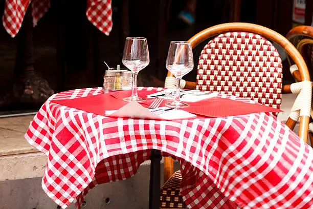 Table dressed for lunch in the outdoor restaurant in Paris, Latin Quarter. Traditional red chequered napkin and red wicker chair.