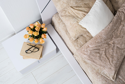 Bright white bedroom interior, cozy bed with beige linen, flowers on a bedside table, shot from above.