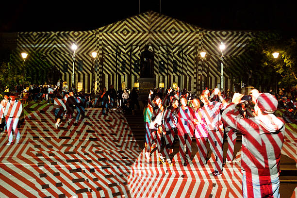 Melbourne, Australia - February 23, 2014: A group of visitors pose for a photo outside the State Library of Victoria, as a striped design is projected onto its facade as part of White Night Melbourne, an all-night arts festival.