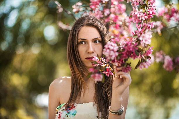 Beautiful smiling young woman wearing a white dress relaxing and enjoying a sunny summer day in the park and carrying a red flower