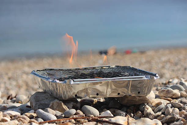 Image of flames on disposable barbecue, charcoal bbq on beach Photo showing some large flames on a disposable barbecue, which has just been lit and is warming up on a pebble beach.  These lumpwood charcoal barbecues are easy to use.  Simply light the paper with a match, through the metal grill, choosing a spot that isn't too windy. Aflame stock pictures, royalty-free photos & images