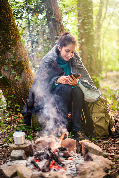 istock young woman sitting near a campfire using her phone 476111734