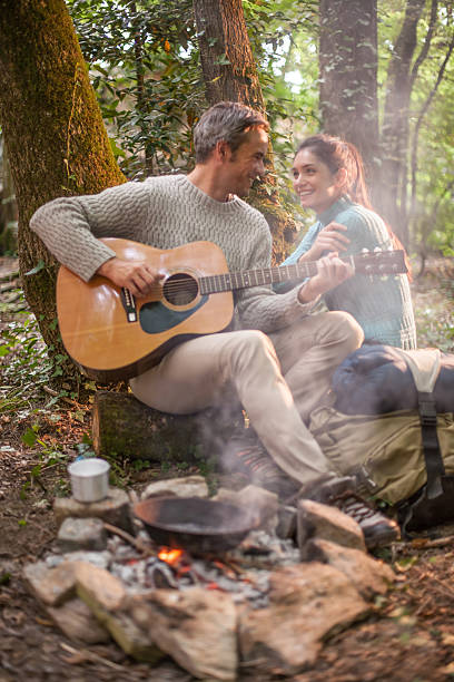 istock couple sitting near a campfire, he plays guitar 476112134