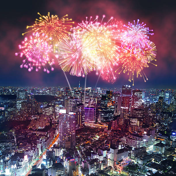 Fireworks show with colorful explosion illuminating a city skyline, with buildings and skyscrapers reflecting the vibrant lights. New Year's celebrations. Dark blue night sky.  Digital composite image including real and digital generated fireworks, superimposed on a cityscape of Tokyo, Japan.