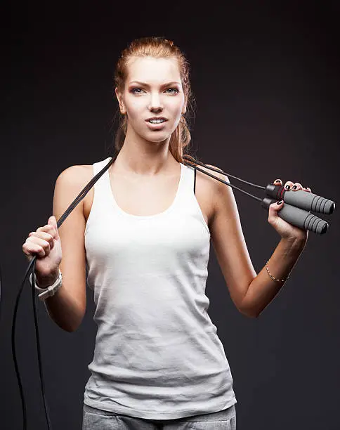 young attractive caucasian girl in white sportswear with jumping-rope on dark background