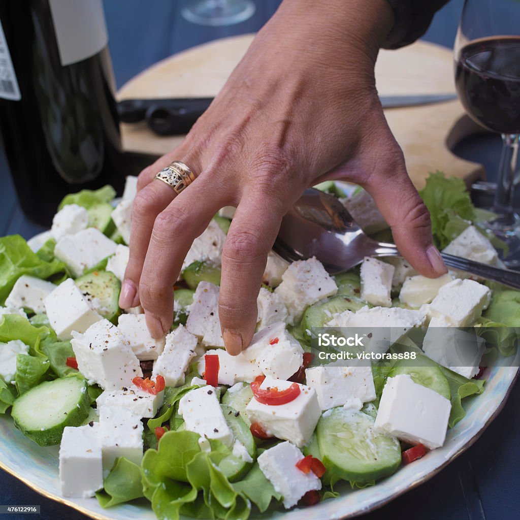 Hand Grabbing Food Closeup of a female hand, grabbing salad, wine bottles in the background 2015 Stock Photo