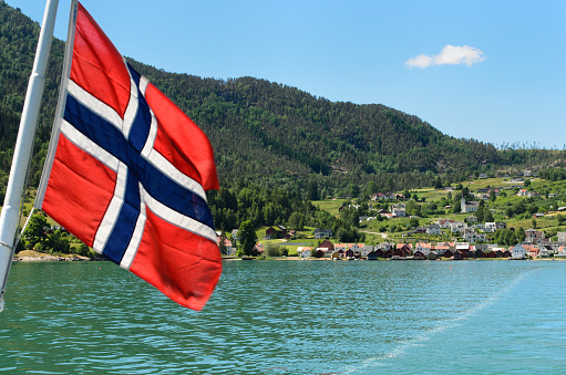 A Norwegian flag on the car ferry from Solvorn to Urnes on the fjord with Solvorn in the background in Sogn og Fjordane, Norway.