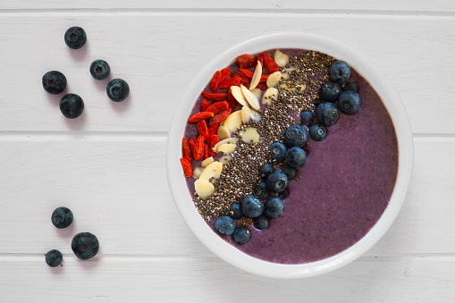 Nutritious blueberry smoothie bowl with goji berries, almonds and chia seeds on white wood with fresh berries