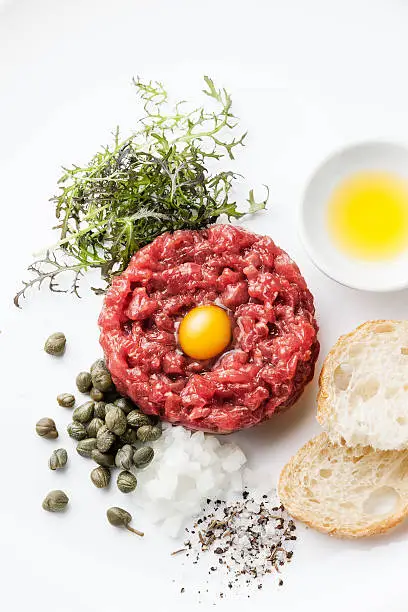 Beef tartare with capers and fresh onions on white background