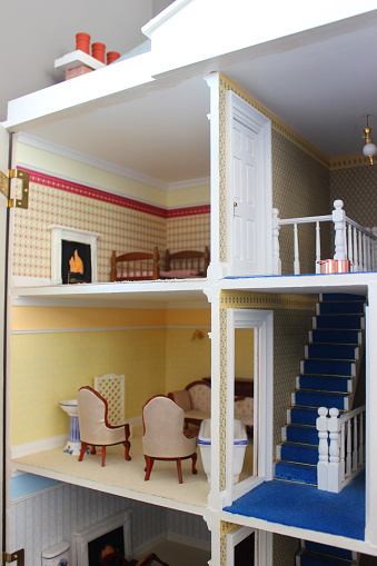 Photo showing the decorated interior of a toy dollshouse, with coloured carpets, working electric lights, walls that have been painted and covered with wallpaper, and a staircase with wooden bannisters / balustrading connecting the different levels.