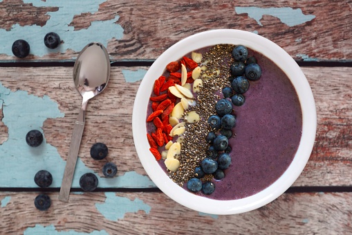 Nutritious blueberry smoothie bowl with goji berries, almonds and chia seeds on a rustic old wood background