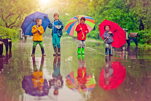 Chilren under umbrella Little boys and girl happily walking under umbrella in park raincoat photos stock pictures, royalty-free photos & images