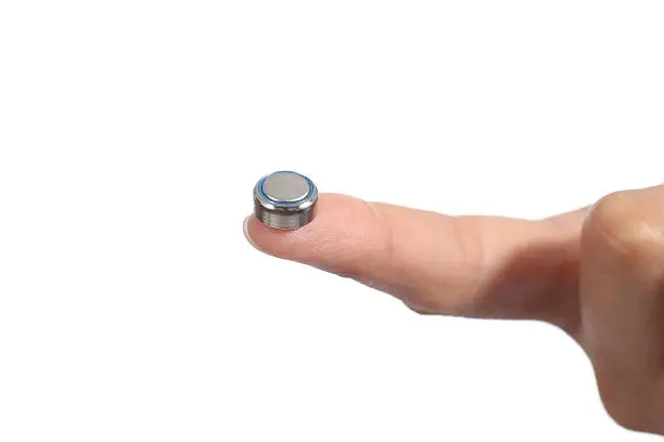 Woman hand holding a button battery with the forefinger isolated on a white background