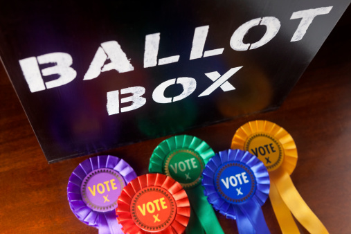 Time to cast your vote in a UK Election. A Ballot Box with coloured rosettes for the principal UK political parties