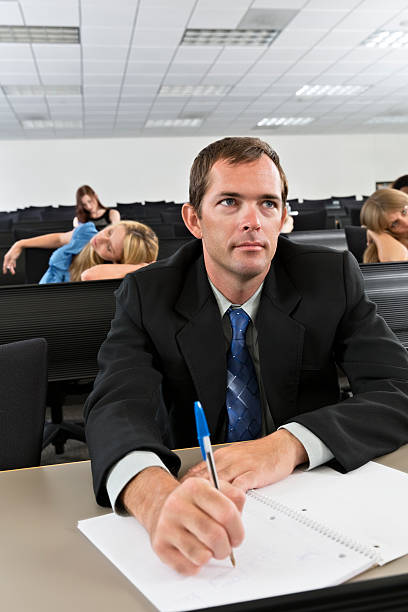 Young Man Only One Paying Attention in Class A young man takes notes while other students are bored in class. male college student sleeping through lecture stock pictures, royalty-free photos & images