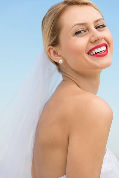A happy charming bride in a white dress with a white veil and a bridesmaid with a pink veil hug gently and smile thoughtfully. Cheerful bachelorette party in the summer park. Close-up portrait.