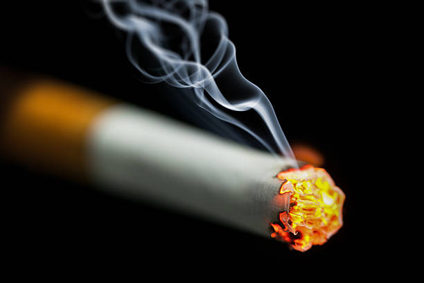 burning cigarette with smoke burning cigarette with smoke on black background cigarette fire stock pictures, royalty-free photos & images