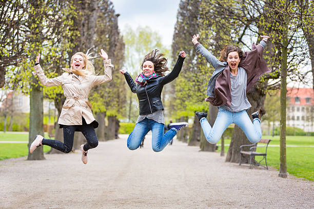 Group of women jumping at park in Copenhagen. They are in their twenties and they are wearing smart casual clothes. Happiness, friendship and success concepts.
