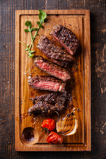 Sliced medium rare grilled Beef steak Ribeye with grilled onions and cherry tomatoes on cutting board on wooden background