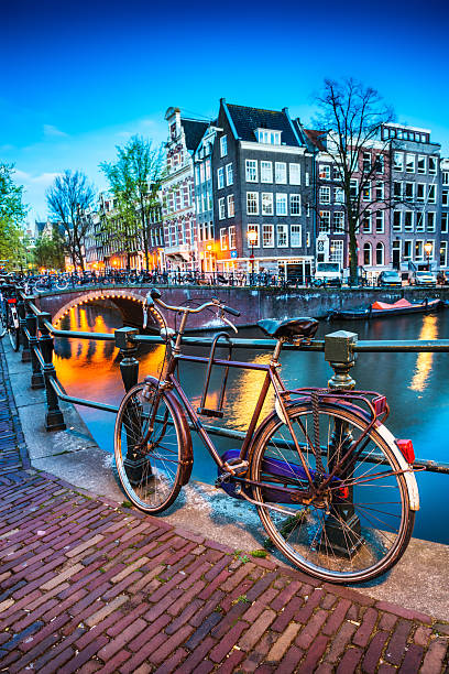 Bridge with Bicycle and Water Channel in Amsterdam at Night Typical Amsterdam City Night Scene. Visible are one of the many beautiful bridges, bikes, street lights, illuminations, reflection in the canal, and traditional dutch houses. Amsterdam, Netherlands. bicycle rack photos stock pictures, royalty-free photos & images