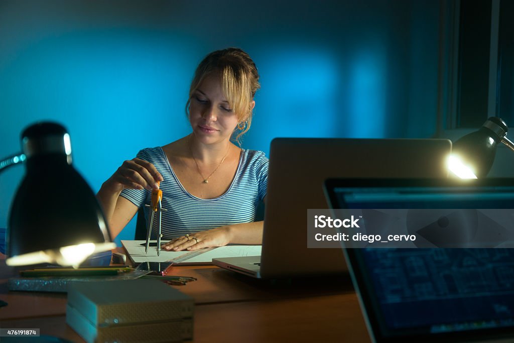 Happy Woman Interior Designer Working Project Drawing Late Night Beautiful woman working as interior designer, staying late at night in office with drawings and laptop computer to complete a project. The girl draws a circle with compasses 2015 Stock Photo