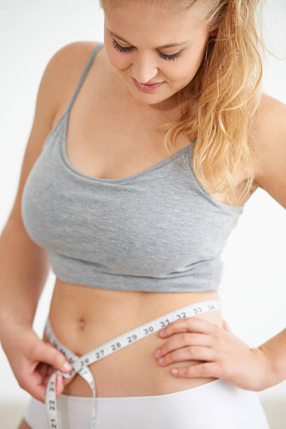 Curvaceous young woman measuring her waistline with a tape measure