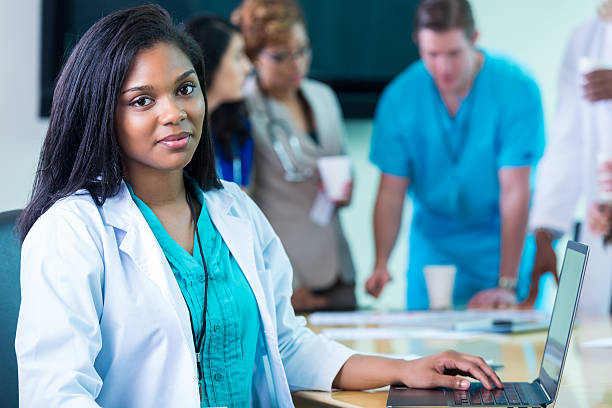 istock African American female doctor using laptop during hospital staff meeeting 476197708