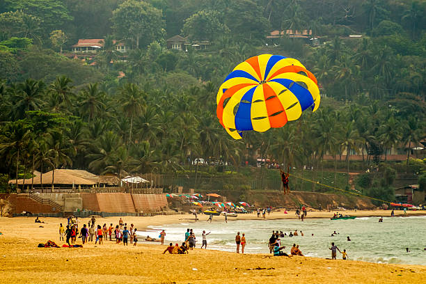 parachuter gliding over a populated beach Candolim, Goa, India - February 15, 2013: Tourists are para-sailing in the sunny sea side of Calangute Beach airborne sport stock pictures, royalty-free photos & images