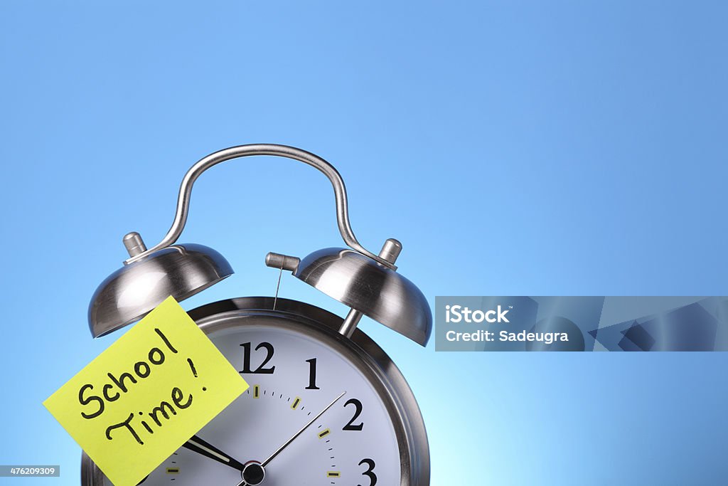 School Time Alarm clock with a yellow adhesive note. In the background a blue chalkboard. Adhesive Note Stock Photo