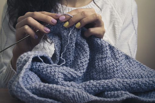 The girl in the white sweater with bright manicure knits blue thread. Vintage photo close up.