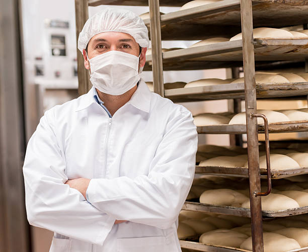 Man working at an industrial bakery Man working at an industrial bakery wearing full uniform - food factory concepts baker occupation stock pictures, royalty-free photos & images