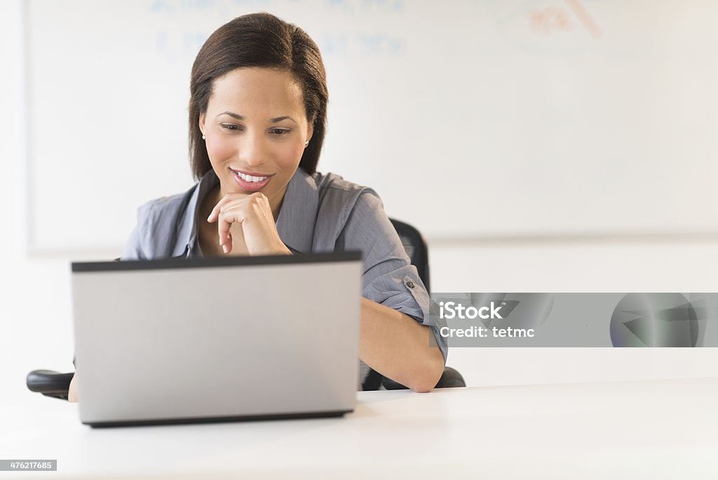 Businesswoman With Hand On Chin Using Laptop At Desk Beautiful young businesswoman with hand on chin using laptop at office desk 20-29 Years Stock Photo