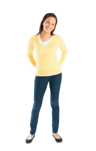 Full length portrait of confident young woman in casuals with hands behind back against while background