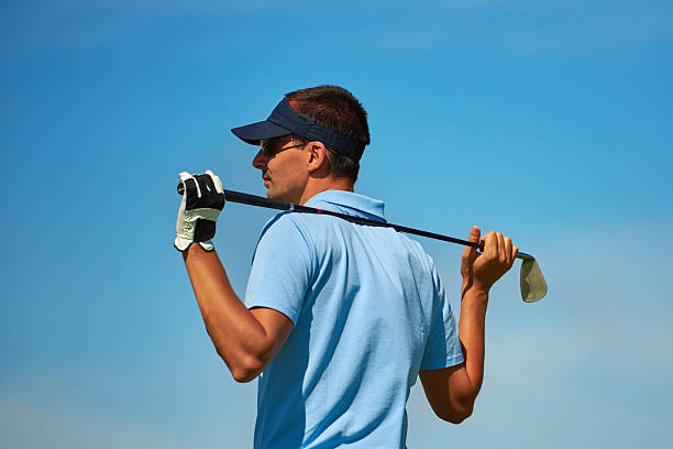 golf player relaxing side view of golf player with golf club behind his head looking away, sky in background. sideways baseball hat stock pictures, royalty-free photos & images