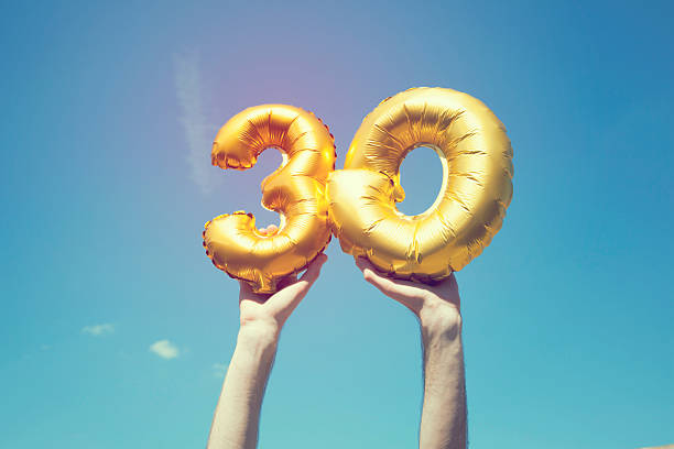 Gold number 30 balloon A gold foil number 30 balloon is held high in the air by caucasian male hand.  The image has been taken outdoors on a bright sunny day, the sky is blue with some clouds. A vintage style effects has been added to the image. 30 34 years stock pictures, royalty-free photos & images