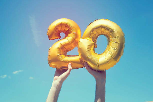 Gold number 20 balloon A gold foil number 20 balloon is held high in the air by caucasian male hand.  The image has been taken outdoors on a bright sunny day, the sky is blue with some clouds. A vintage style effects has been added to the image. 20 24 years stock pictures, royalty-free photos & images