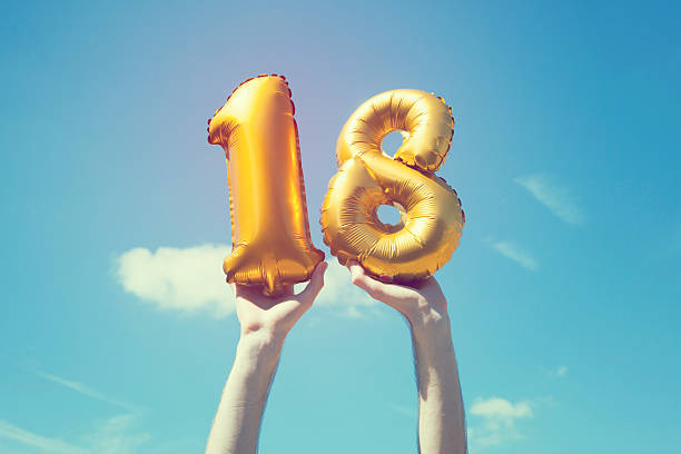 Gold number 18 balloon A gold foil number 18 balloon is held high in the air by caucasian male hand.  The image has been taken outdoors on a bright sunny day, the sky is blue with some clouds. A vintage style effects has been added to the image. 18 19 years stock pictures, royalty-free photos & images