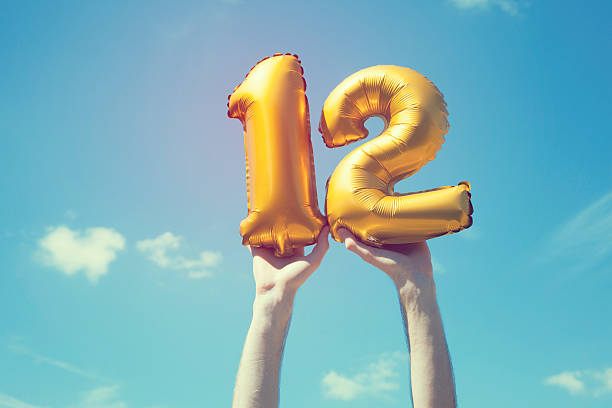 Gold number 12 balloon A gold foil number 12 balloon is held high in the air by caucasian male hand.  The image has been taken outdoors on a bright sunny day, the sky is blue with some clouds. A vintage style effects has been added to the image. number 12 photos stock pictures, royalty-free photos & images