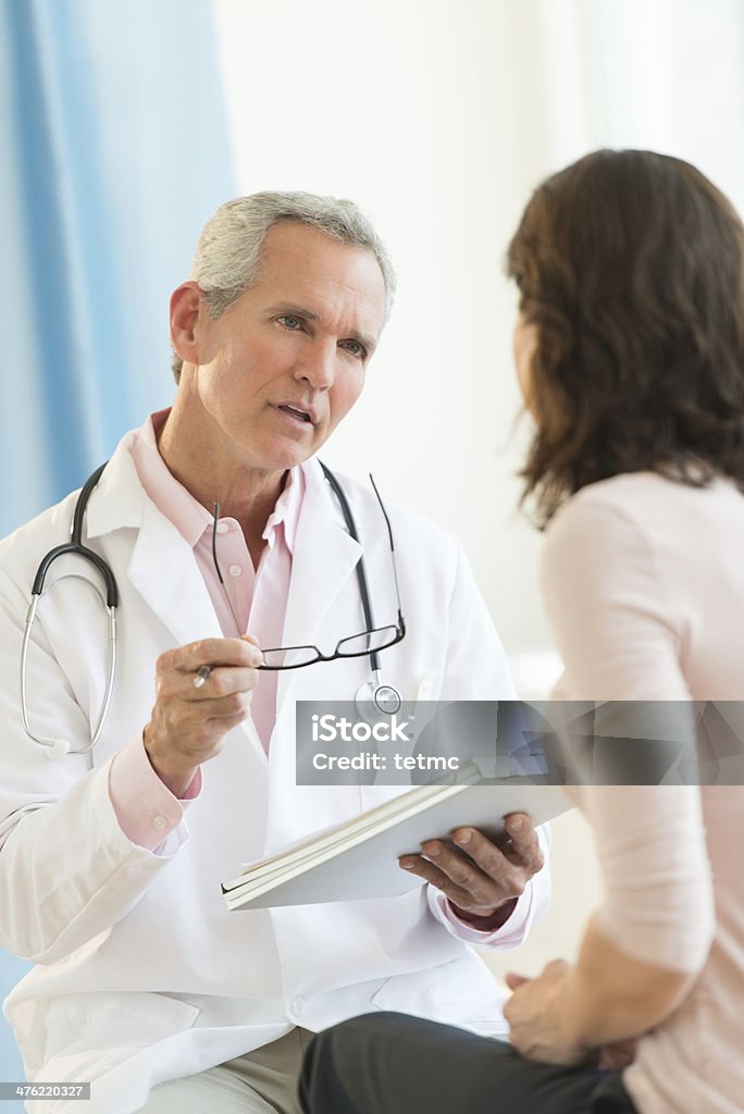 Doctor Communicating With Female Patient Mature male doctor communicating with female patient in hospital Patient Stock Photo