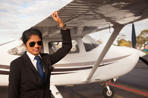 A pilot leaning against the wing of an aircraft. The pilot is a young woman of Indian ethnicity. The aircraft is a Cessna.
