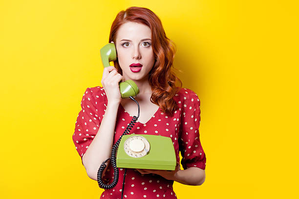 girl in red dress with green dial phone Surprised redhead girl in red polka dot dress with green dial phone on yellow background. red dress photos stock pictures, royalty-free photos & images