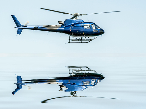 Helicopter flying on blue sky, and reflection in the water