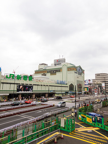 Tokyo, Japan - August 16, 2014: Top view of construction site across the Shinjuku train station with big street in front the station. The pavement is going trough construction site which is fool of yellow lines for blind people.  In background are surrounding buildings. Above is grey cloudy sky.