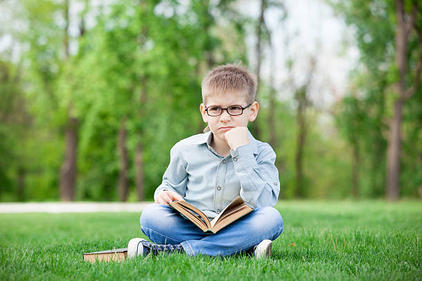 istock sad boy with book on green grass 476234554