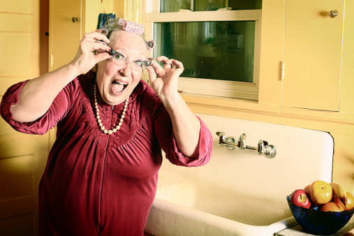 A crazy granny in curlers and cat's eye glasses in her kitchen near the sink. More granny images.